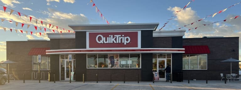 QuikTrip storefront with red and white sign, pennant banners strung overhead and a sunny sky.